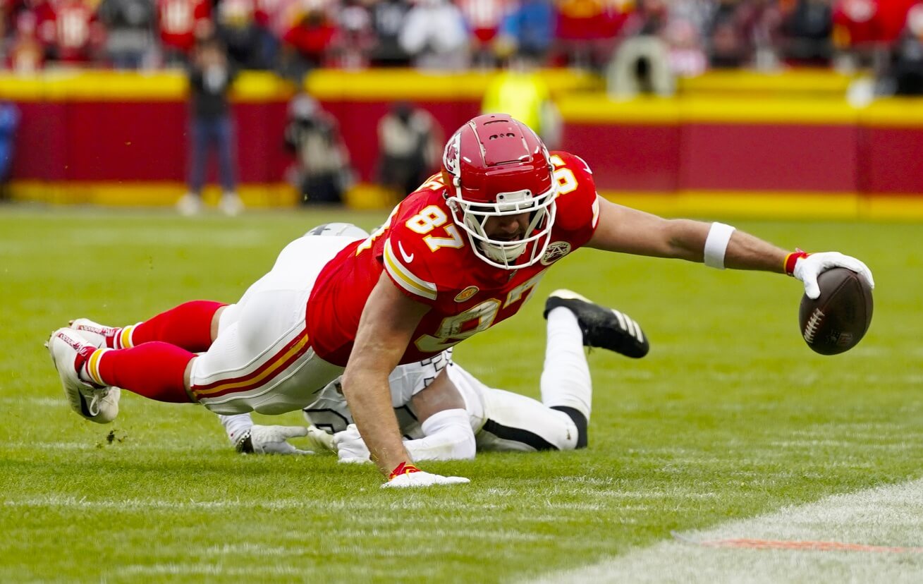 Dec 25, 2023; Kansas City, Missouri, USA; Kansas City Chiefs tight end Travis Kelce (87) dives for the sideline against Las Vegas Raiders cornerback Nate Hobbs (39) during the first half at GEHA Field at Arrowhead Stadium. Mandatory Credit: Jay Biggerstaff-USA TODAY Sports